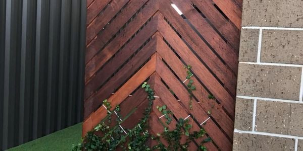 Timber panelled garden screen with climbing plants, surrounded by synthetic turf, steel fence and brick wall