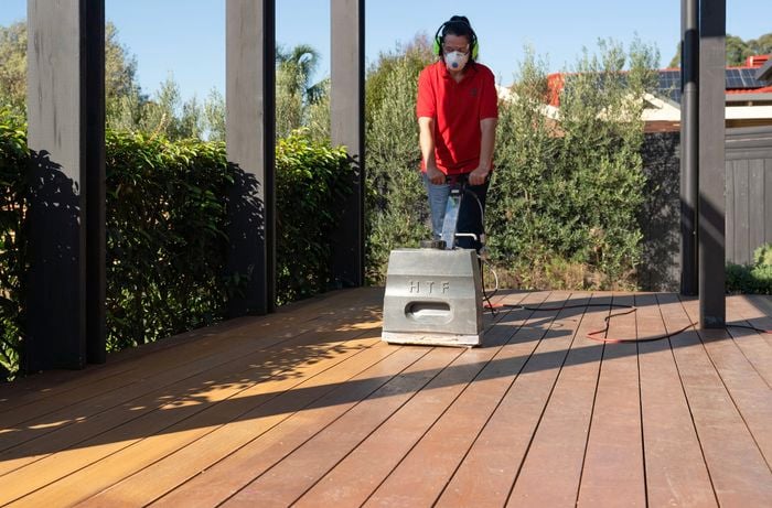  A Bunnings Team Member is using a drum floor sander and safety gear to sand a timber deck surface before refinishing.