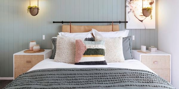 Bedroom with green wall panelling and bed with lots of cushions.