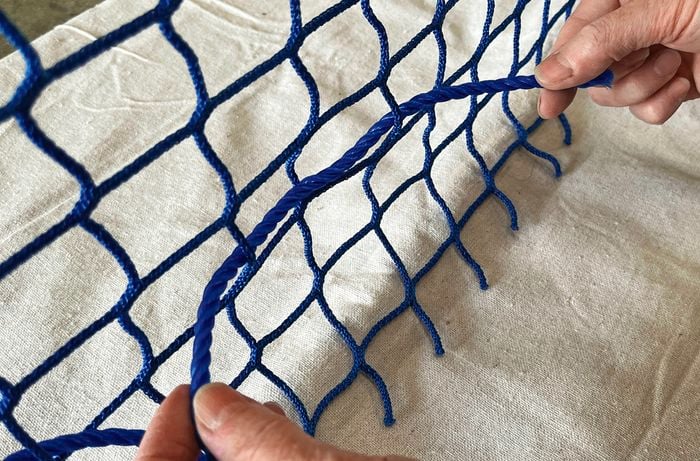 Hands thread a blue rope through a blue cargo net.