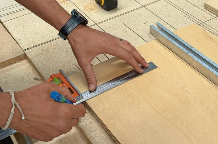 Hands using a ruler and pencil to mark a line on a piece of plywood.