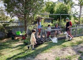 Three adults and two children chatting around a gated garden.