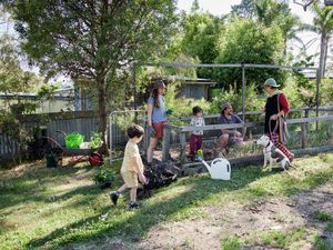 Three adults and two children chatting around a gated garden.