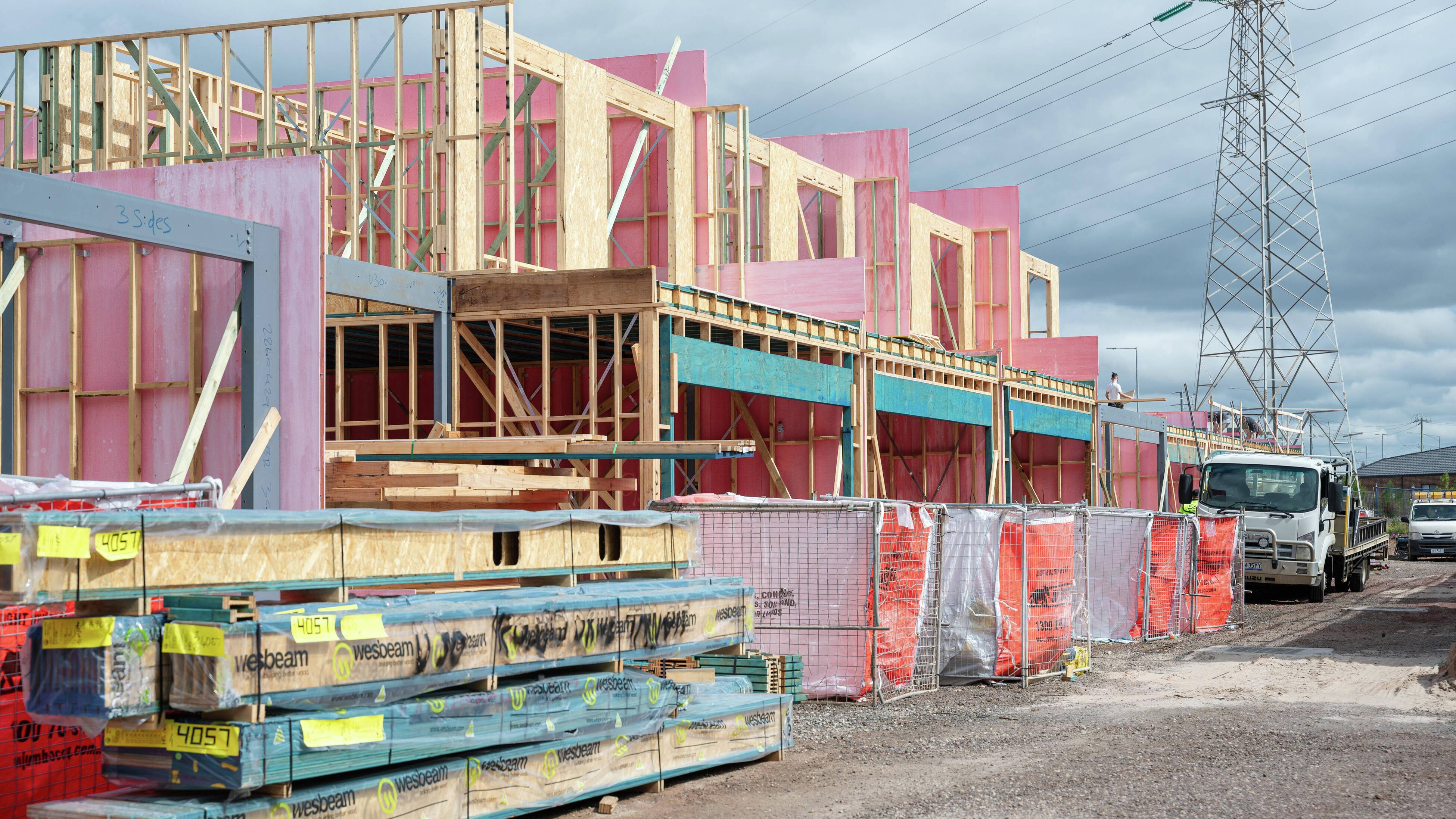 A man wearing a black Bunnings Trade shirt walks alongside a building site at frame and truss stage