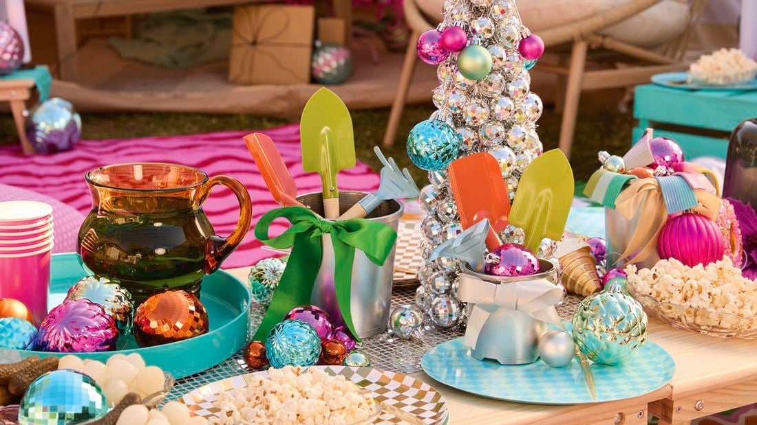 A table decorated with a silver bauble tree, colourful ornaments, small garden tools in silver buckets and plates of popcorn.