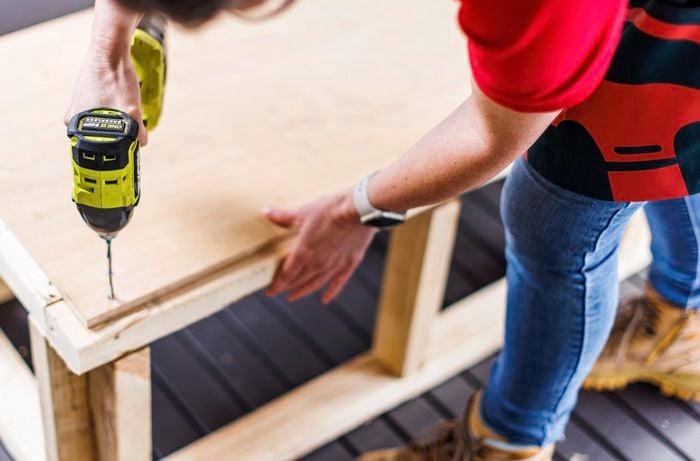 A person drilling a sheet of marine ply to the bottom of the frame.