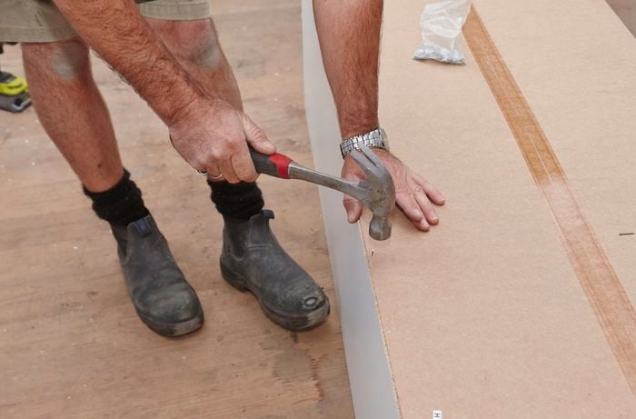 Person hammering nail to secure back and side panels of wardrobe insert unit together.