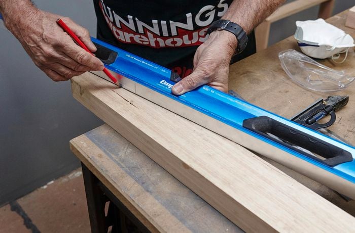 A spirit level and a pencil being used to rule an angled cut marker into a piece of timber