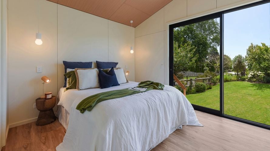 Bright bedroom with large sliding glass doors, timber ceiling and garden views.