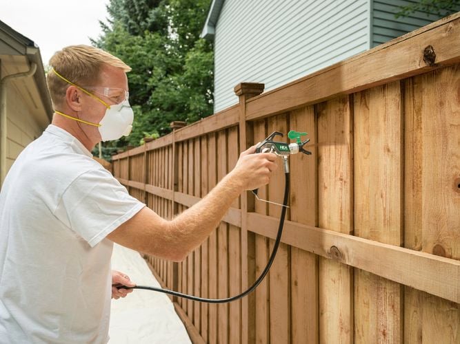 Wagner Control Pro Hybrid Gun with HEA tip spraying a fence with brown paint.