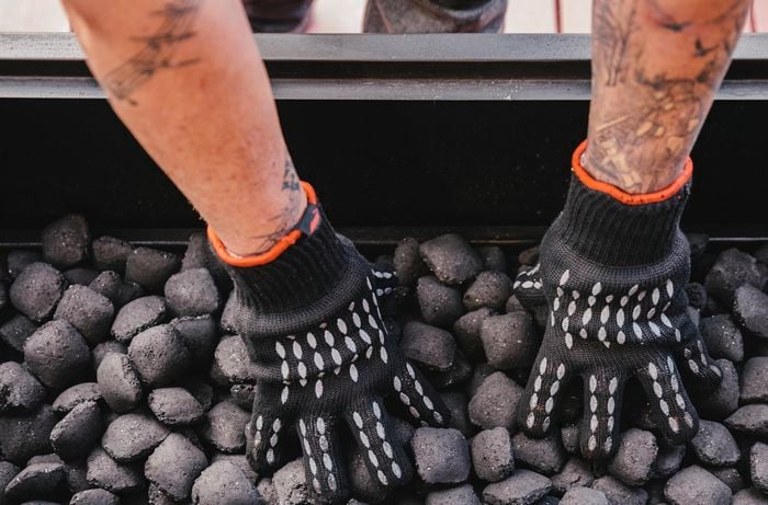 Person spreading charcoal beads in a spit roaster