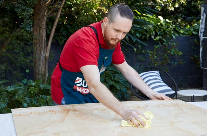 Person wiping plywood sheet with a cloth.