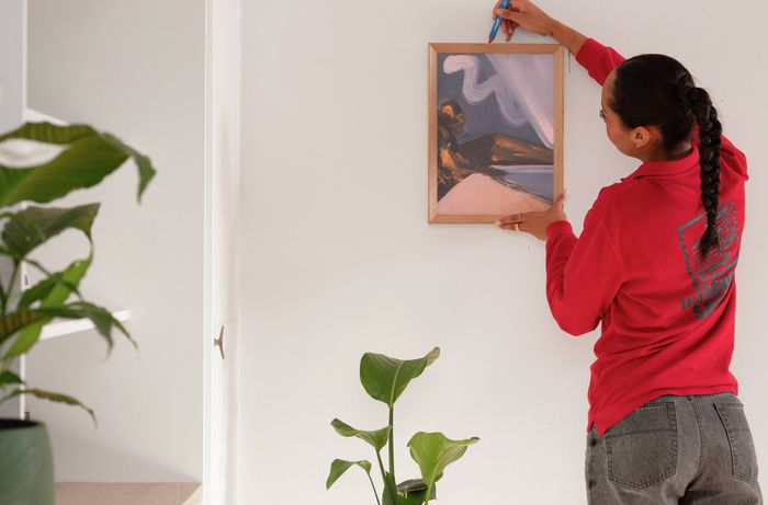 A Bunnings Team Member is checking the position of framed wall art and marking the wall to help accurately place the picture hanger. 