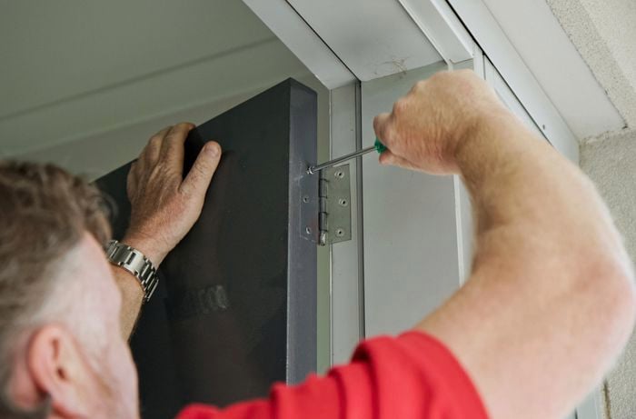 Person using a screwdriver to remove door hinges.