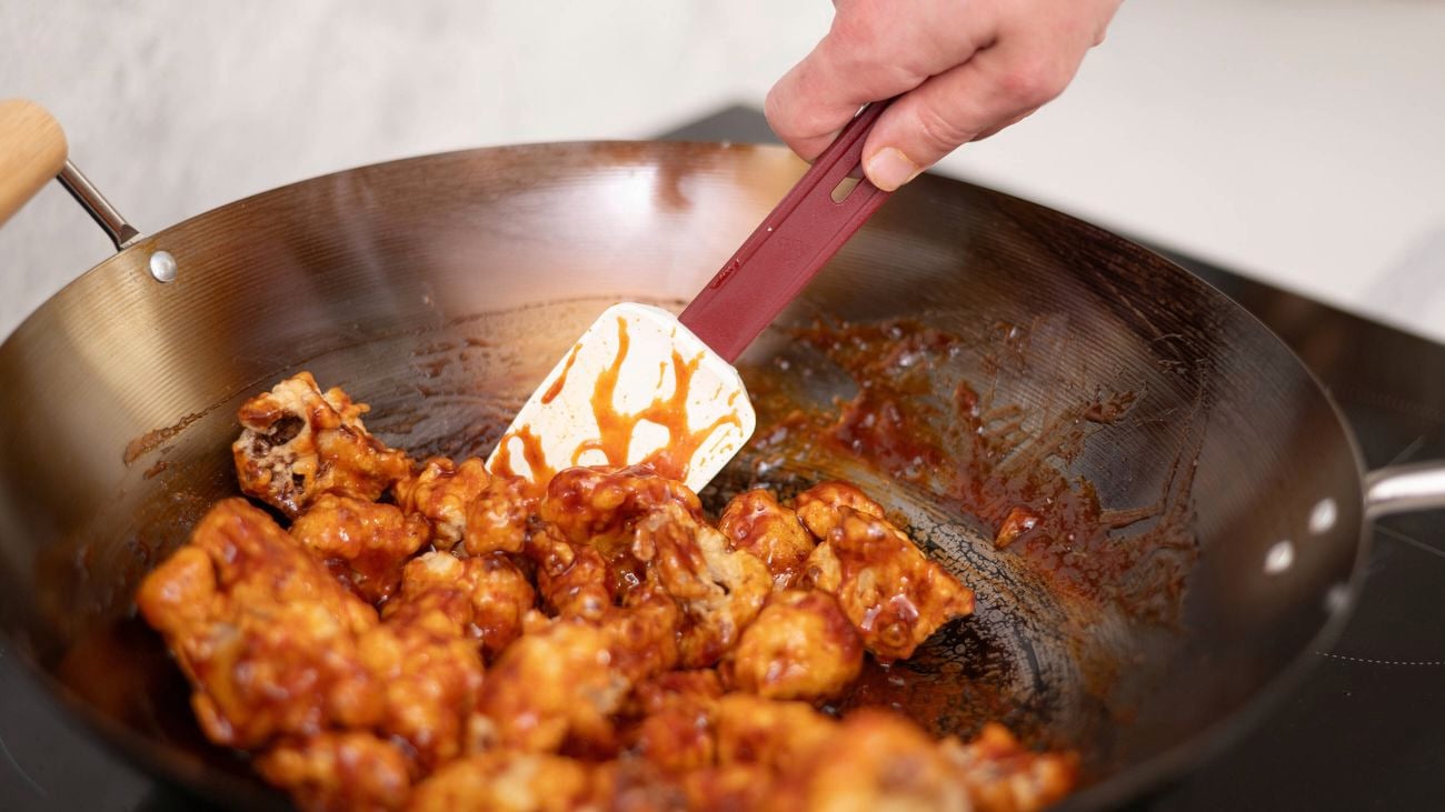 A hand is tossing cauliflower to evenly coat it in a tasty, sticky glaze