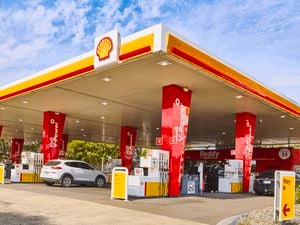A shell petrol station with two cars parked in it.