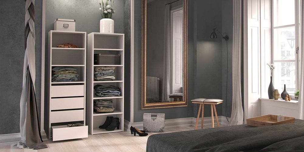 A bedroom with two shelving units against a wall, a bed, a mirror on the wall and a stool in it.