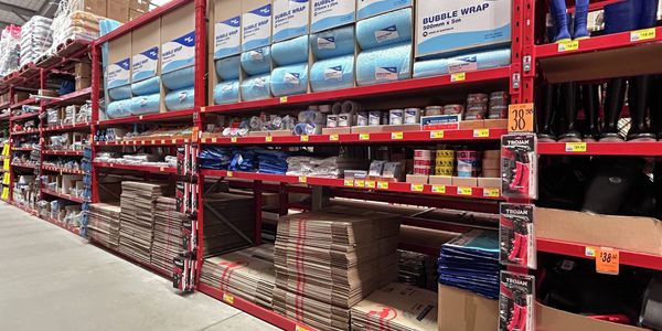 Pool and spa maintenance aisle in a hardware store, featuring shelves stocked with pool chemicals, water treatment products, testing supplies and cleaning equipment displayed on red industrial racking.