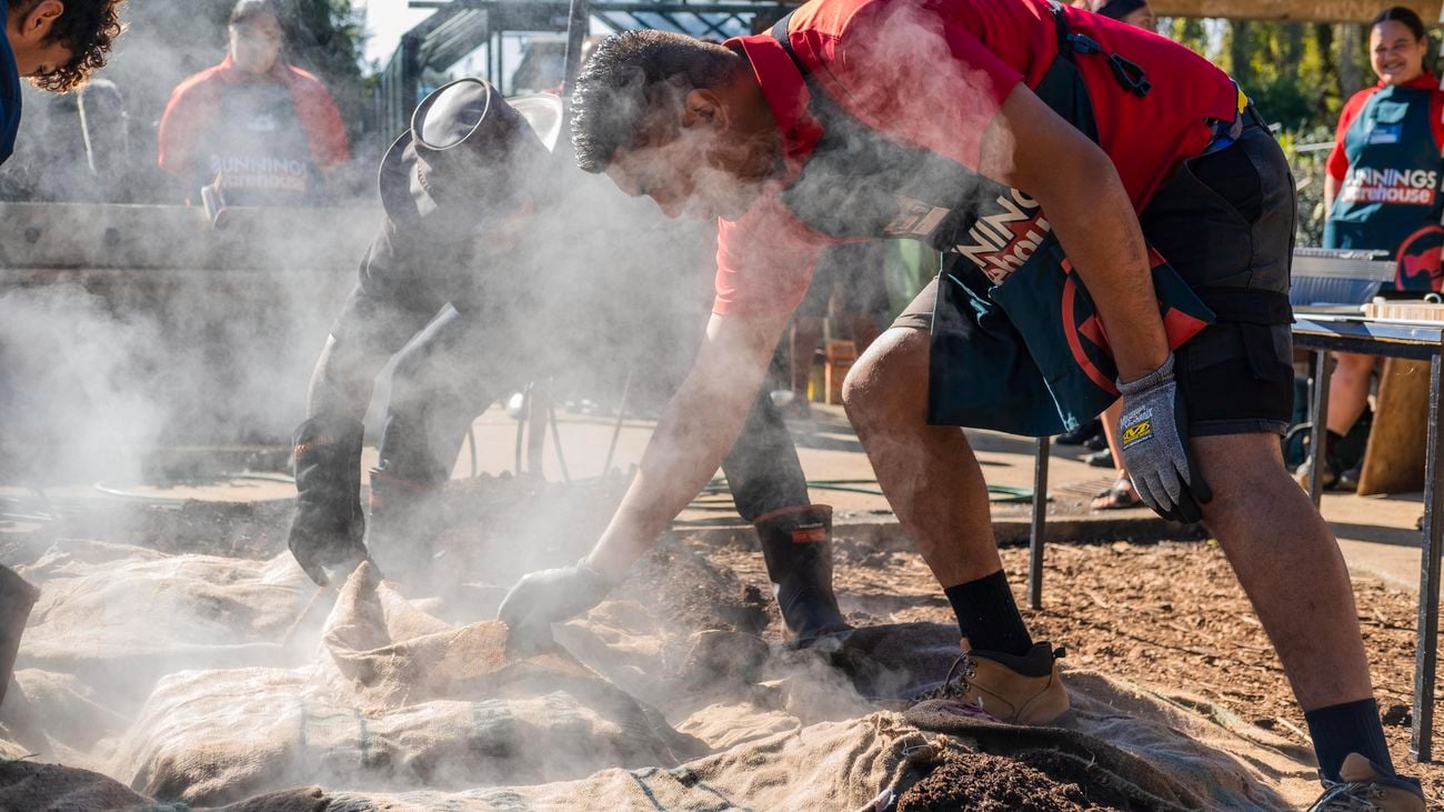 A person standing over a hangi, with smoke coming out of it.