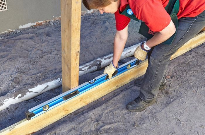 Person placing spirit level on top of piece of timber plinth.