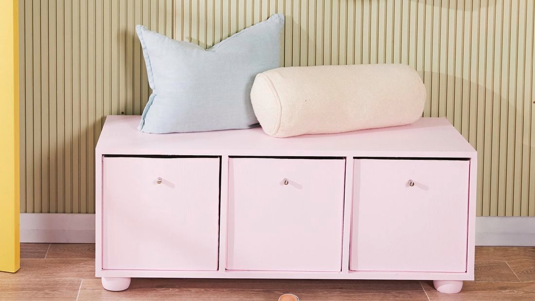 Pinked coloured hallway storage cabinet with several cushions neatly arranged on top of it.