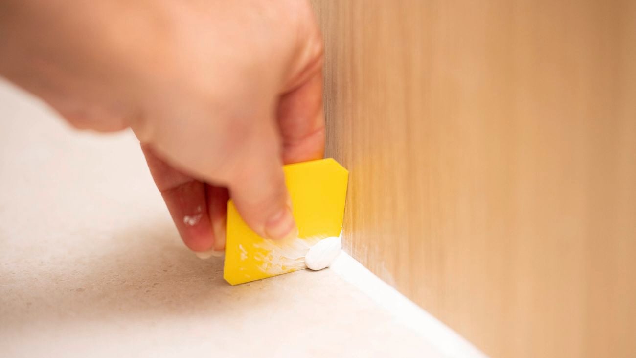 A person is using a removal edge of a smoothing tool to remove excess gap filler
