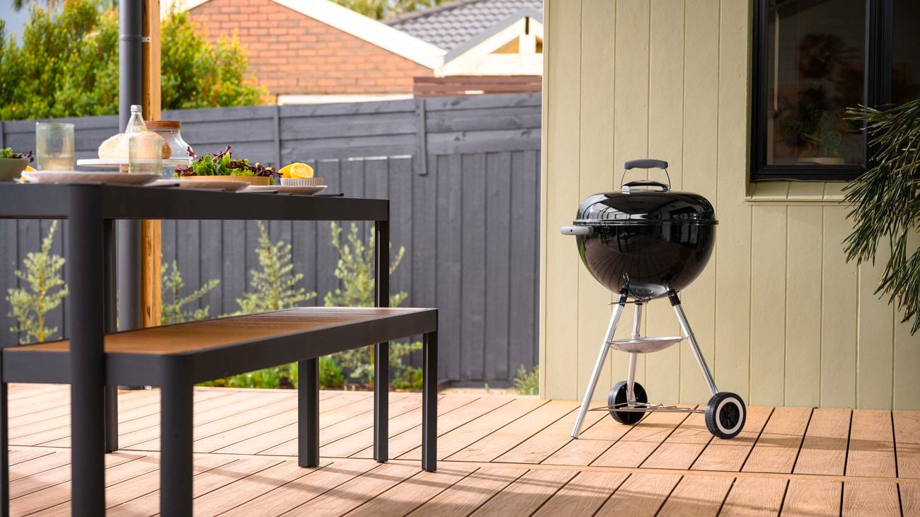 Weber charcoal BBQ on an outdoor deck next to a table setting.