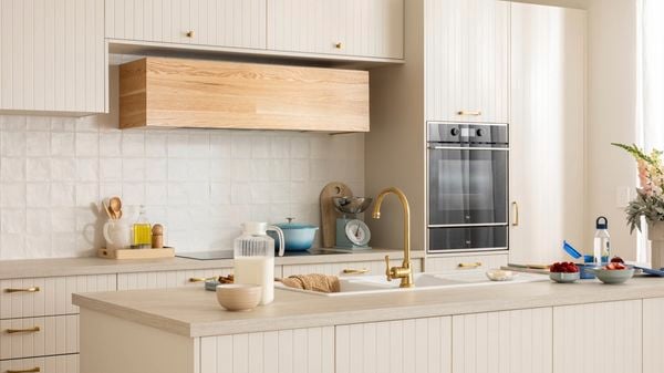 Beige modern kitchen with a brown benchtop, gold sink mixer, crockery and a milk jug on the bench.