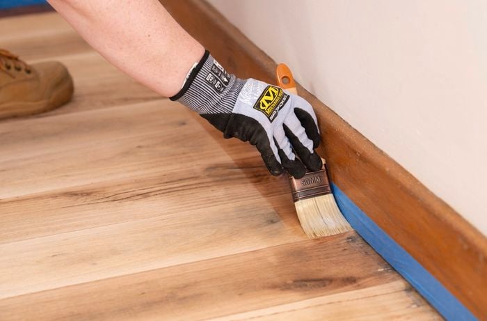 A person is carefully applying sealer along the skirting board to create a smooth transition into the main floor coat. ​