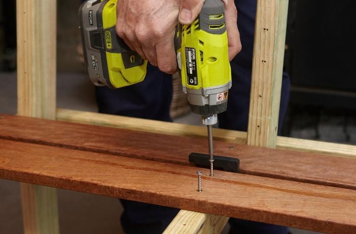 Person drilling screws into seat part of wooden DIY garden bench.