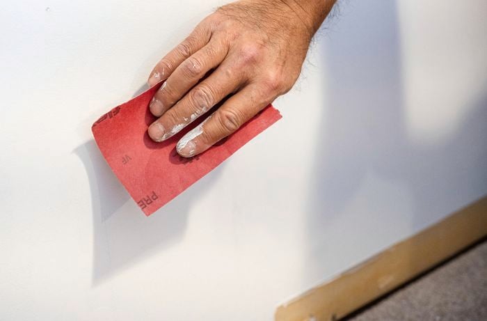 A person holding a piece of sandpaper against a wall