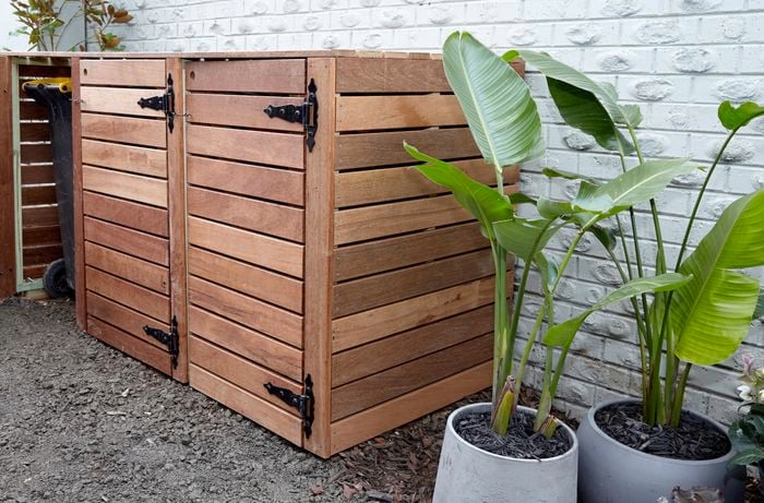 Bin storage unit made of timber, with plants beside.
