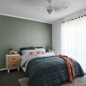 Bedroom with green wall panelling, bed, bedside table and sheer curtains.