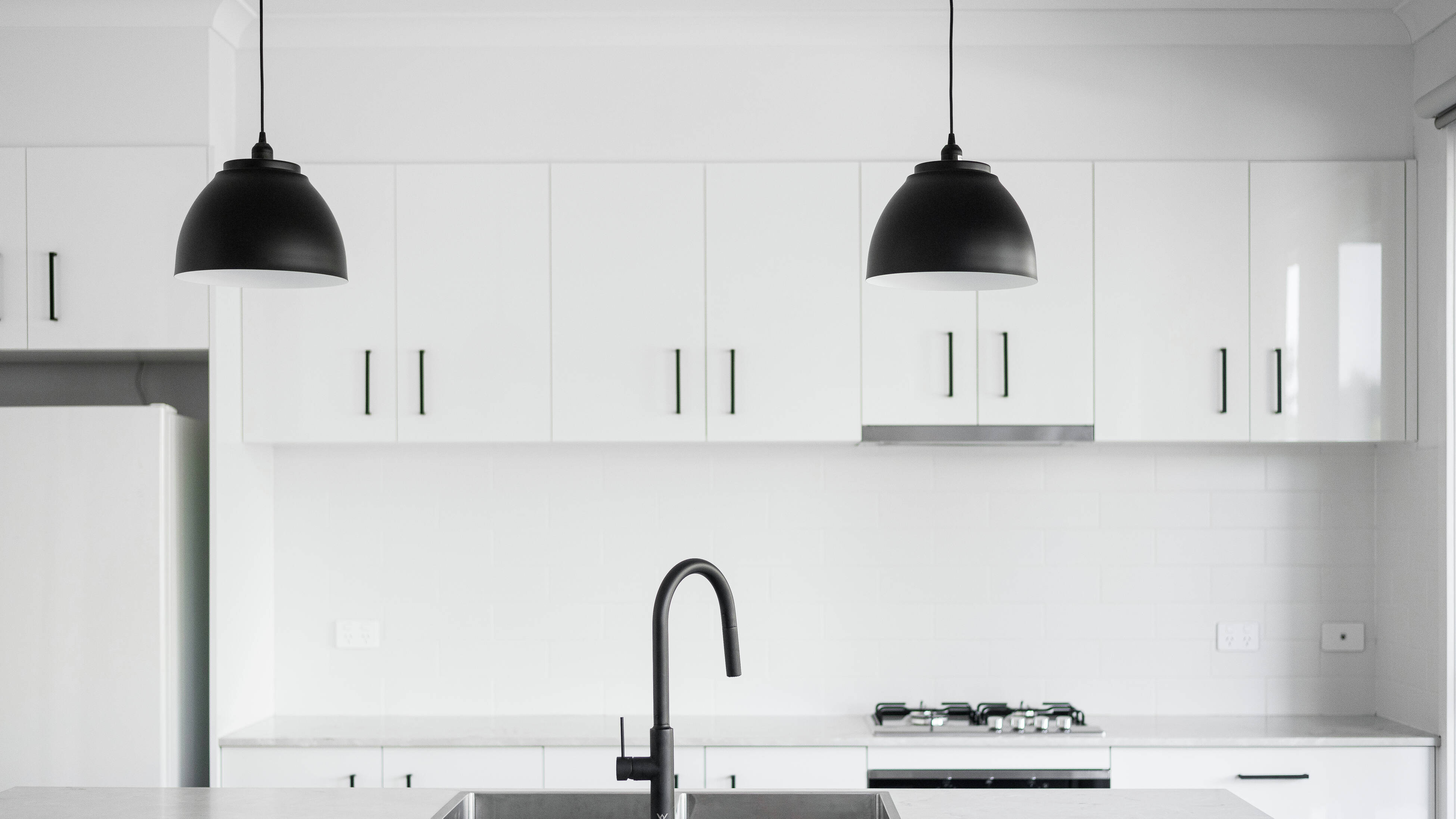 A close-up shot of a new white kitchen installation, with black handles and two black light pendants hanging from the ceiling 