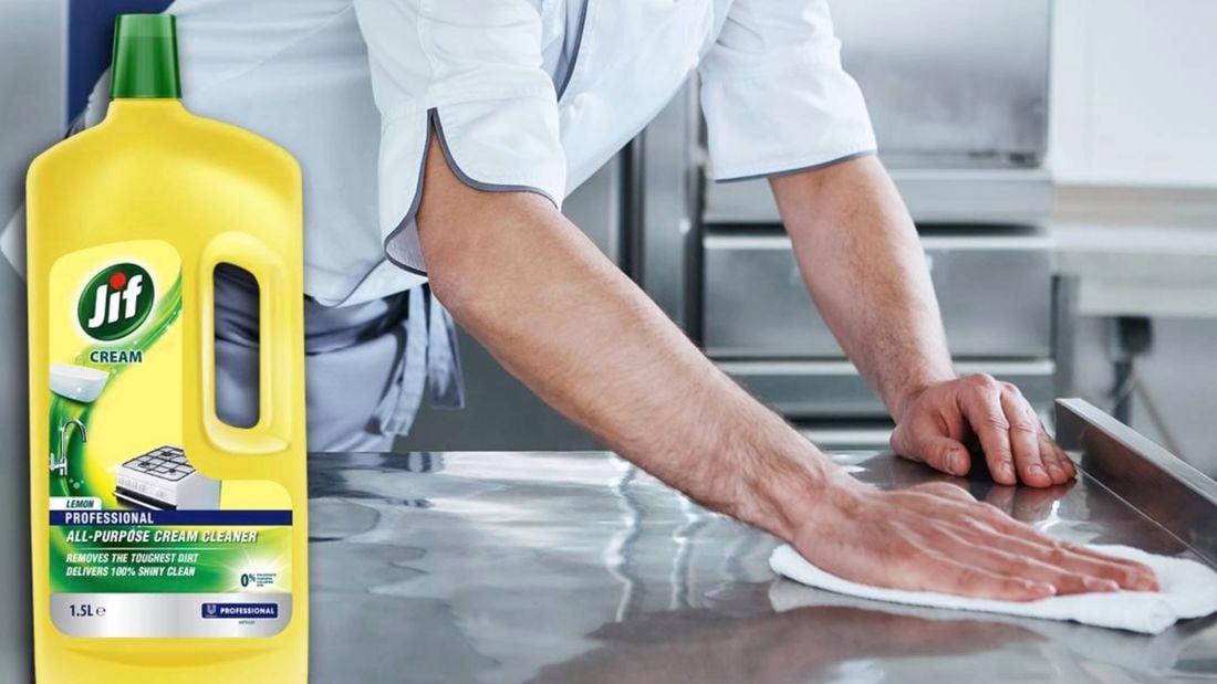 A man’s arms cleaning a stainless steel kitchen bench with a bottle of Jif cream cleanser in the foreground