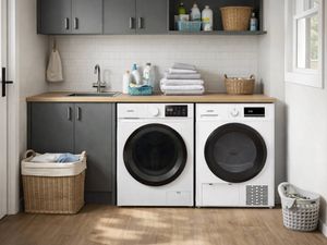 Modern laundry with grey cabinetry, wooden benchtop, and two front‑loading machines side by side beneath a sink, featuring folded towels, cleaning bottles, wicker baskets, and a laundry hamper on timber flooring beside a window.