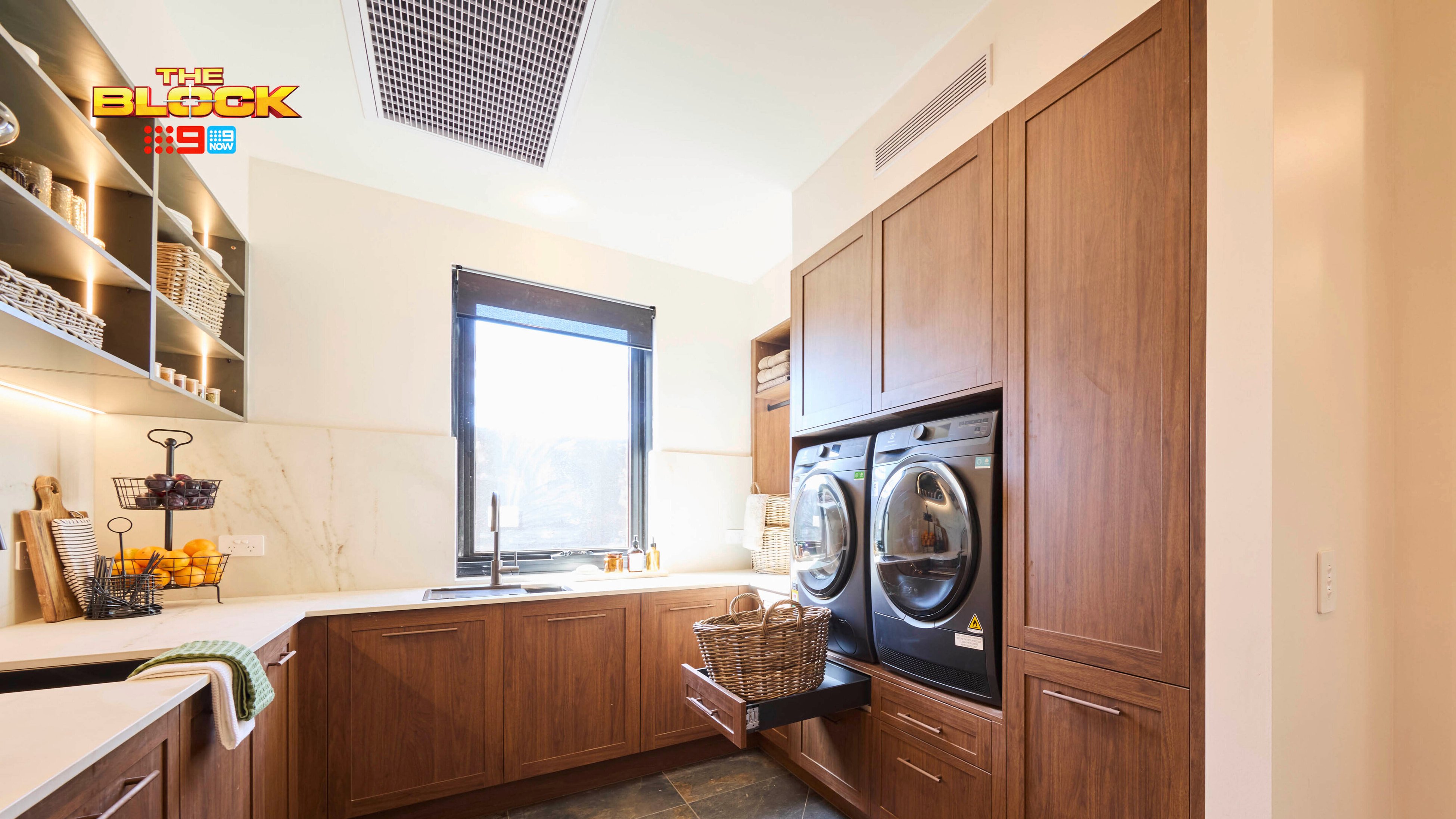 Laundry room from The Block with timber cabinetry, stacked washer and dryer, large sink, and open shelving.