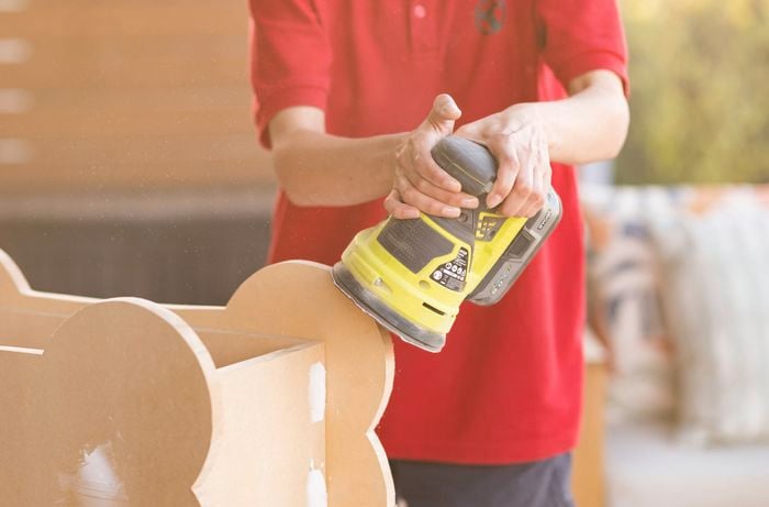 Using Orbital sander to smooth out the edges of a bone shaped dog toy box.