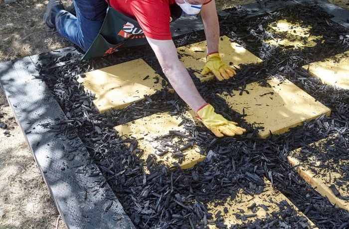 A person spreading black mulch between pavers laid out in a square on a bed of sand
